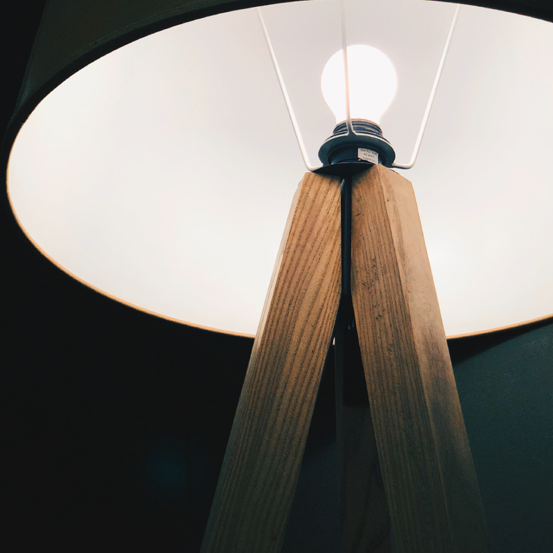 lampadaire trépied en bois avec une ampoule allumé et un abbat jour circulaire blanc en bois